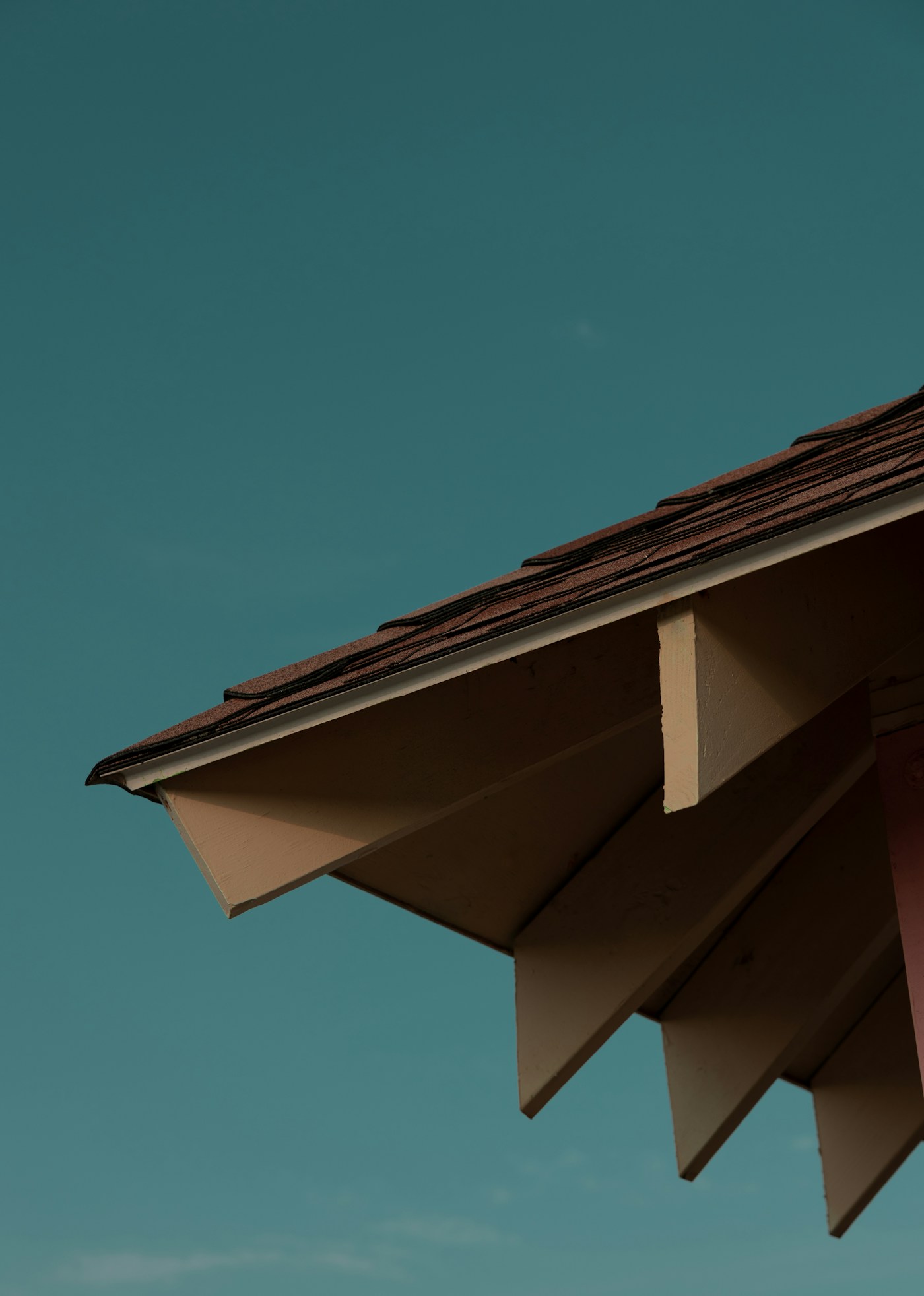 Close-up of a dark shingle roof edge and gutter against a blue sky